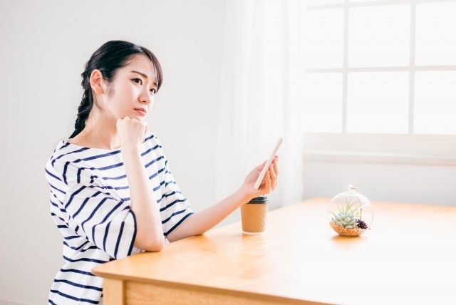 スマホを持ち考えている女性
